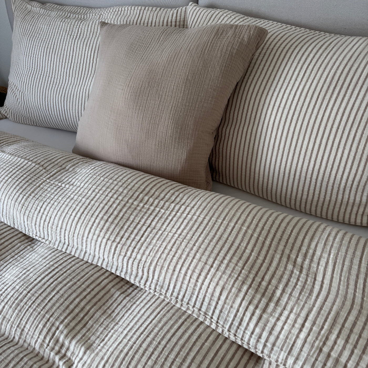 Gestreifte Bettwäsche mit weissem Fixleintuch und Kissen, dazu passender Duvetbezug in Taupe und Ecru auf dem Bett