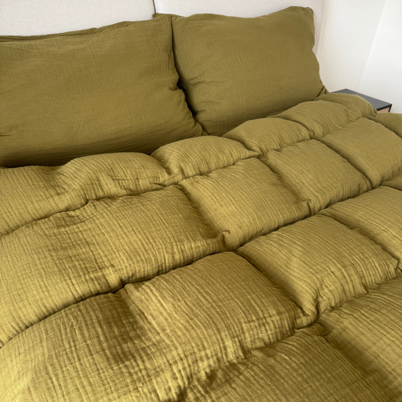 Olivgrüne Bettwäsche ausgebreitet auf dem Bett mit weichem Musselinlook