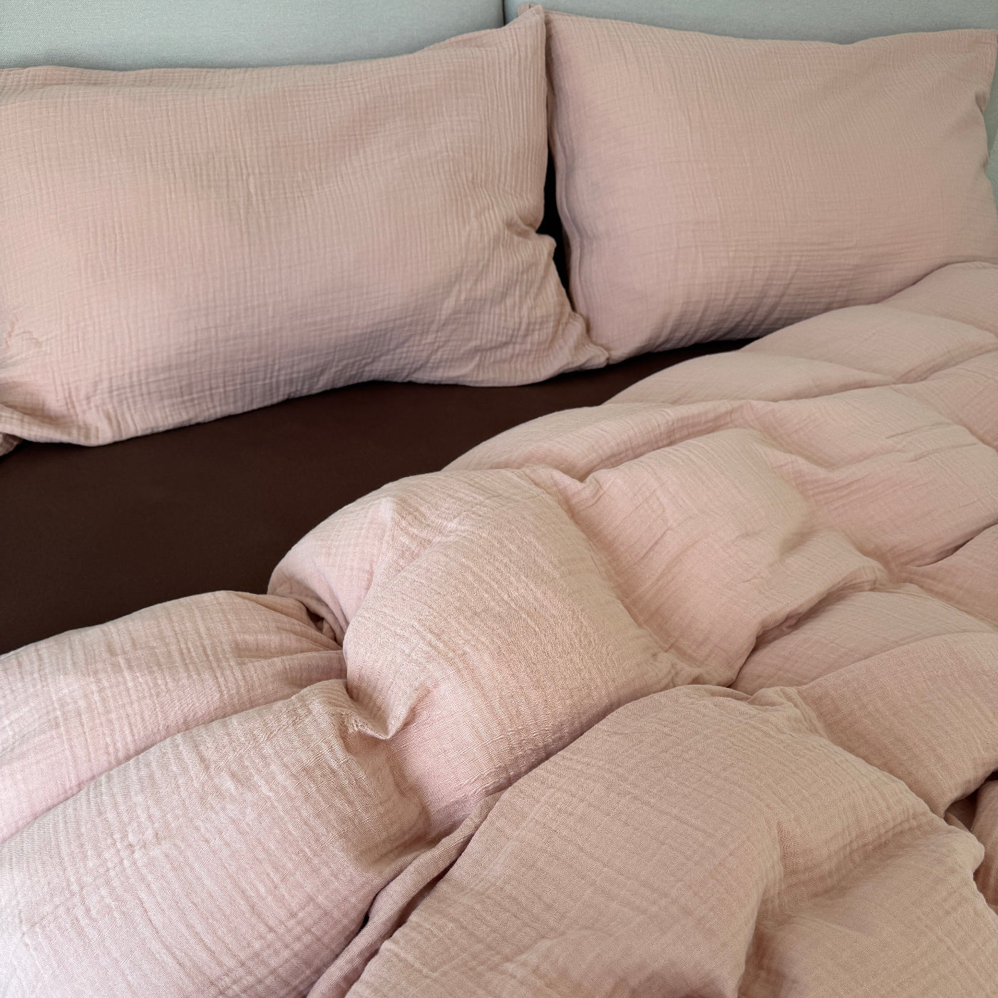 Puderrosa Musselin Bettwäsche mit mokkafarbenem Fixleintuch ausgebreitet auf dem Bett